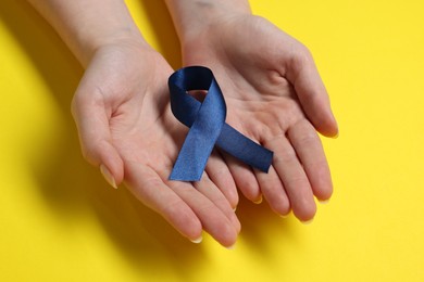 Photo of Woman with dark blue ribbon on yellow background, closeup. Arthritis disease and colon cancer awareness