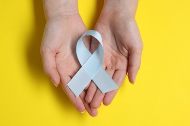 Photo of Woman with light blue ribbon on yellow background, top view. Childhood cancer awareness