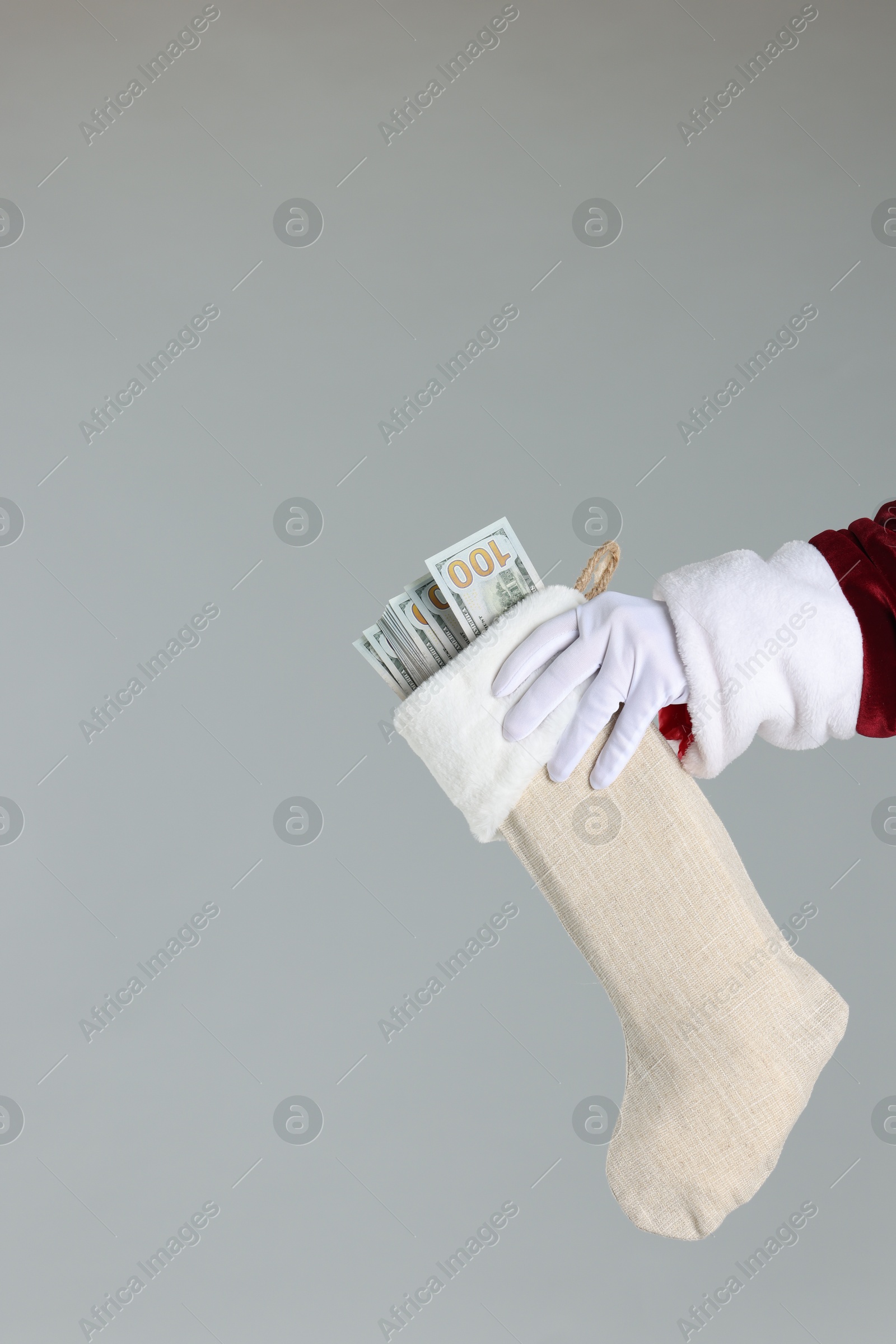 Photo of Santa Claus holding stocking with dollar banknotes on gray background, closeup