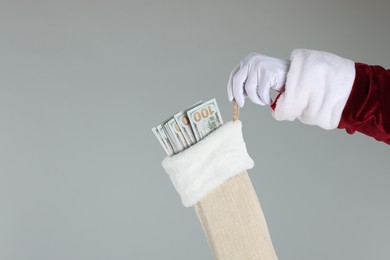 Photo of Santa Claus holding stocking with dollar banknotes on gray background, closeup