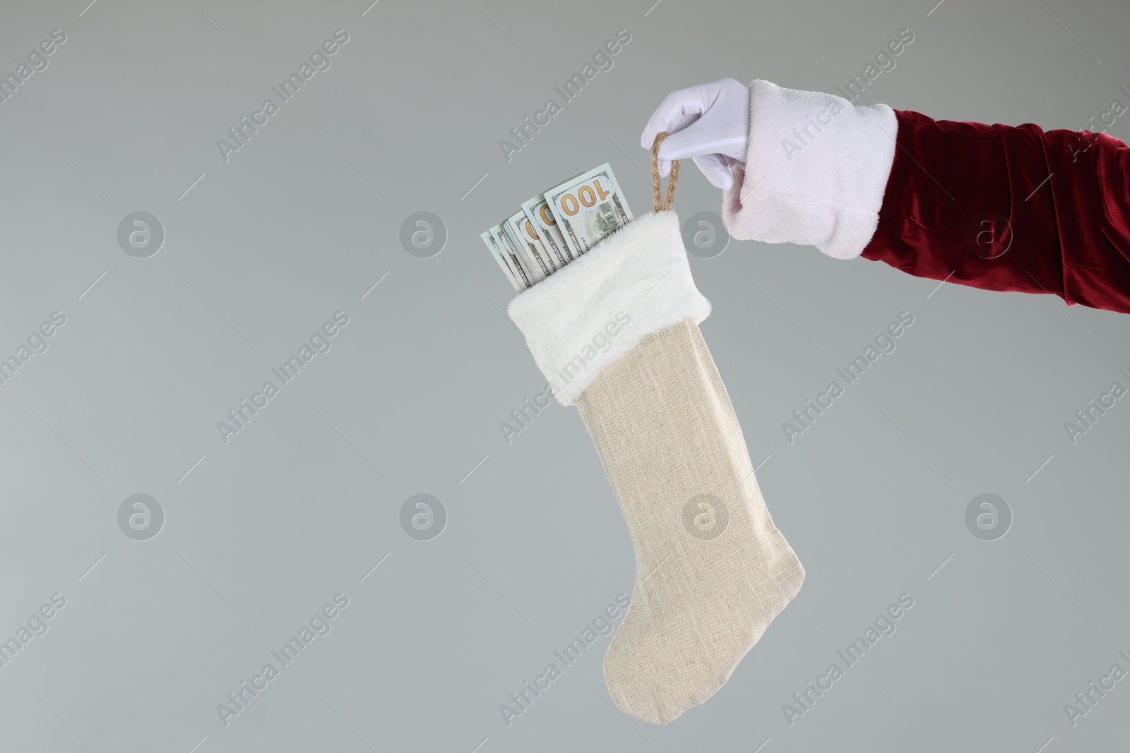 Photo of Santa Claus holding stocking with dollar banknotes on gray background, closeup. Space for text