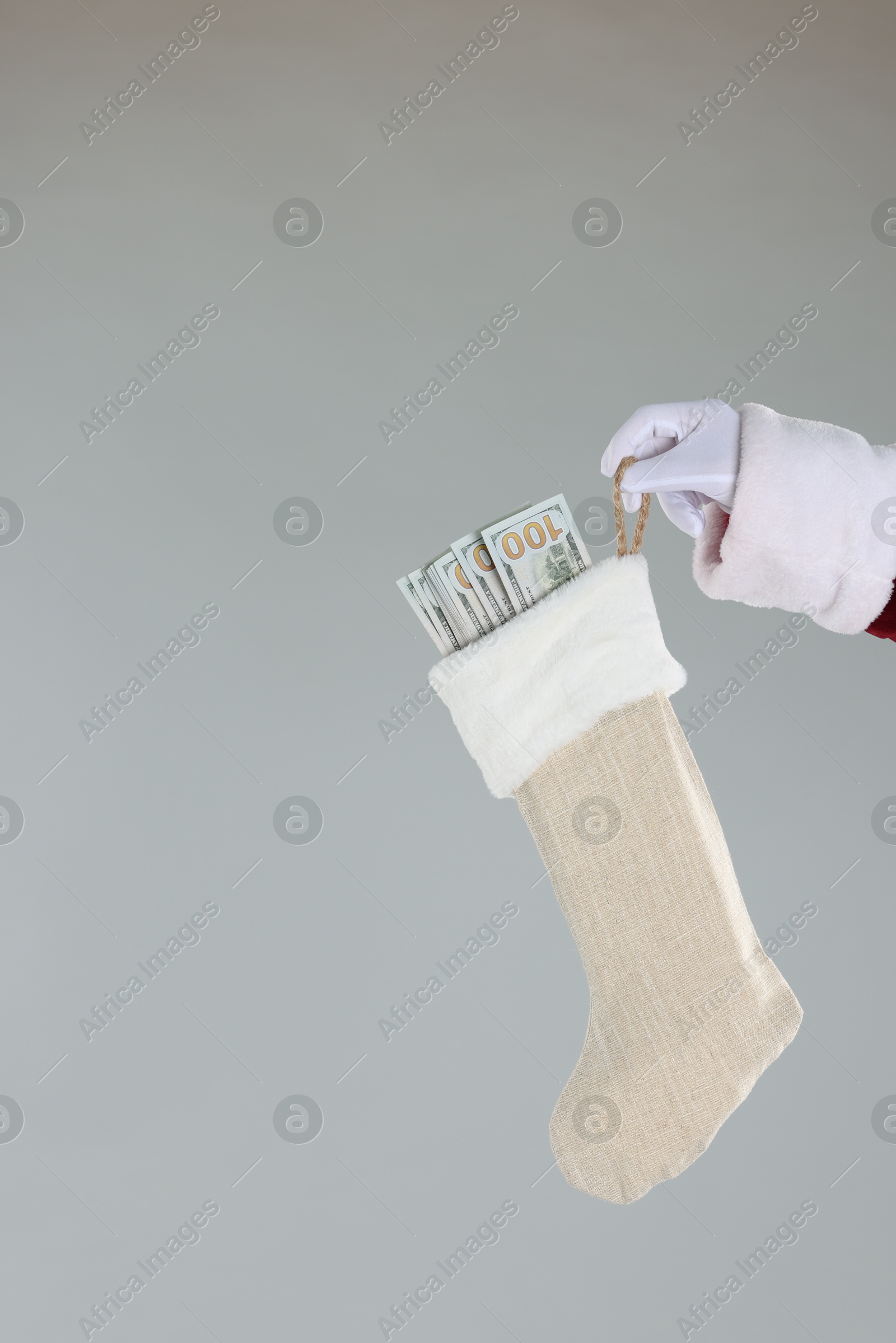 Photo of Santa Claus holding stocking with dollar banknotes on gray background, closeup