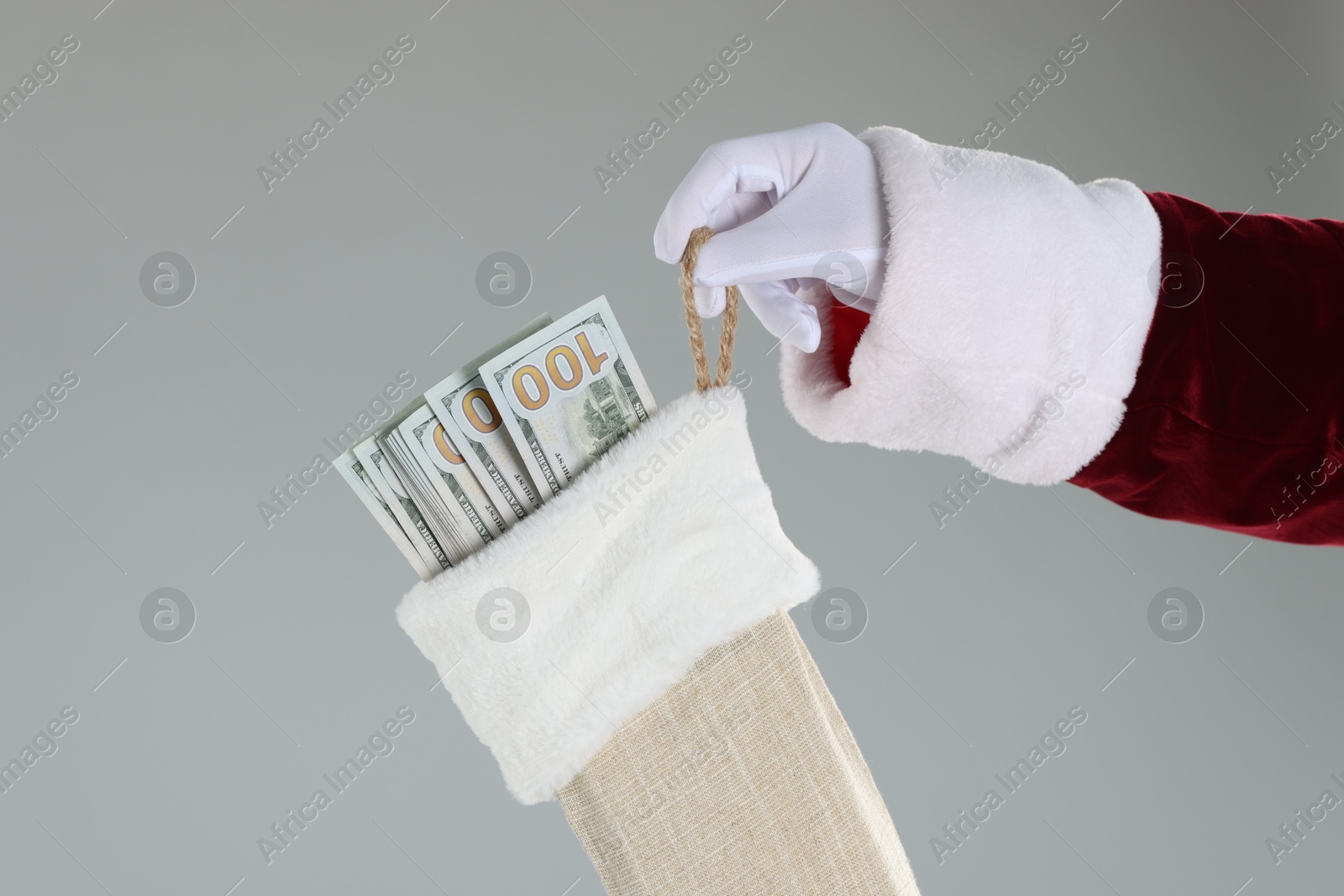 Photo of Santa Claus holding stocking with dollar banknotes on gray background, closeup