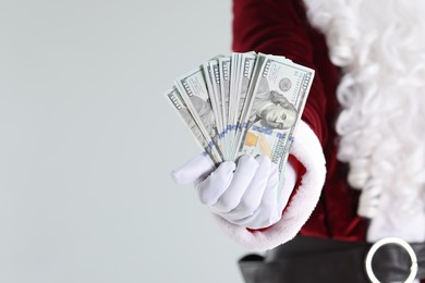 Photo of Santa Claus holding dollar banknotes on gray background, closeup. Space for text