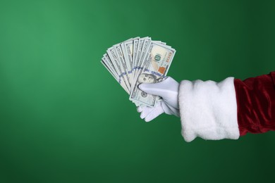 Photo of Santa Claus holding dollar banknotes on green background, closeup. Space for text