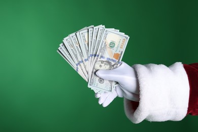 Photo of Santa Claus holding dollar banknotes on green background, closeup. Space for text