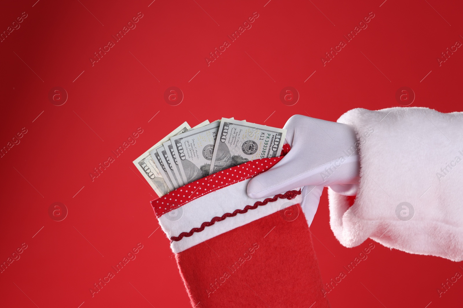 Photo of Santa Claus holding stocking with dollar banknotes on red background, closeup. Space for text