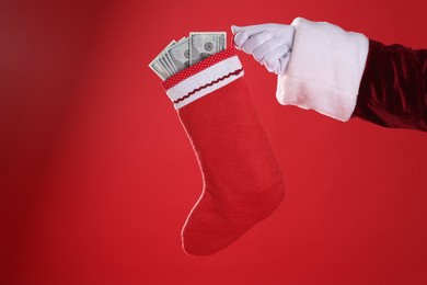 Photo of Santa Claus holding stocking with dollar banknotes on red background, closeup. Space for text