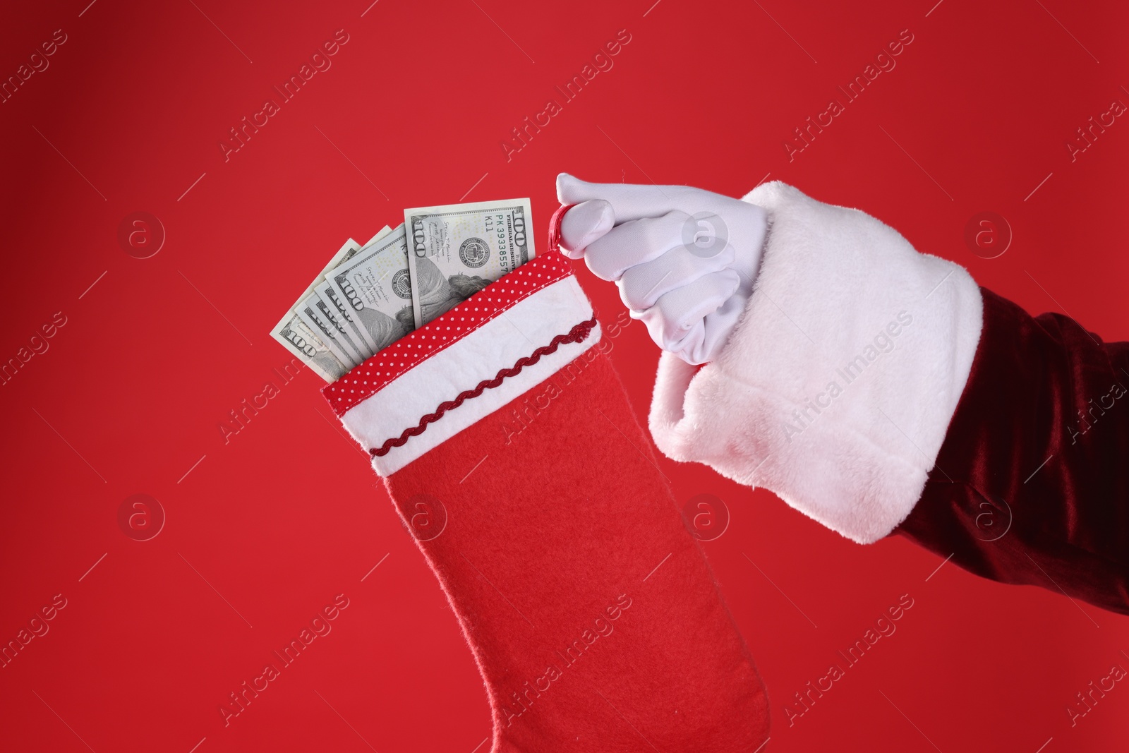 Photo of Santa holding stocking with dollar banknotes on red background, closeup