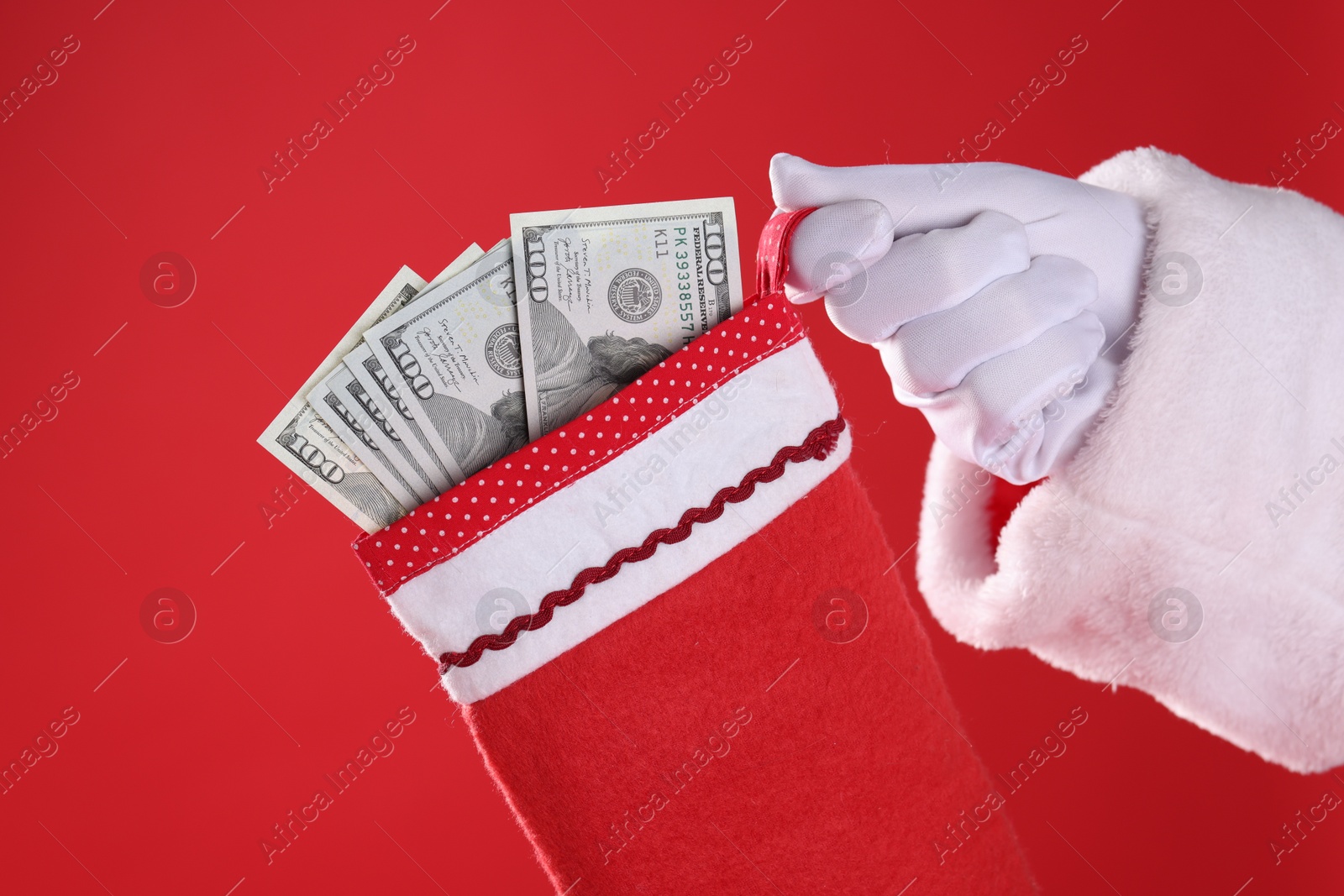 Photo of Santa holding stocking with dollar banknotes on red background, closeup