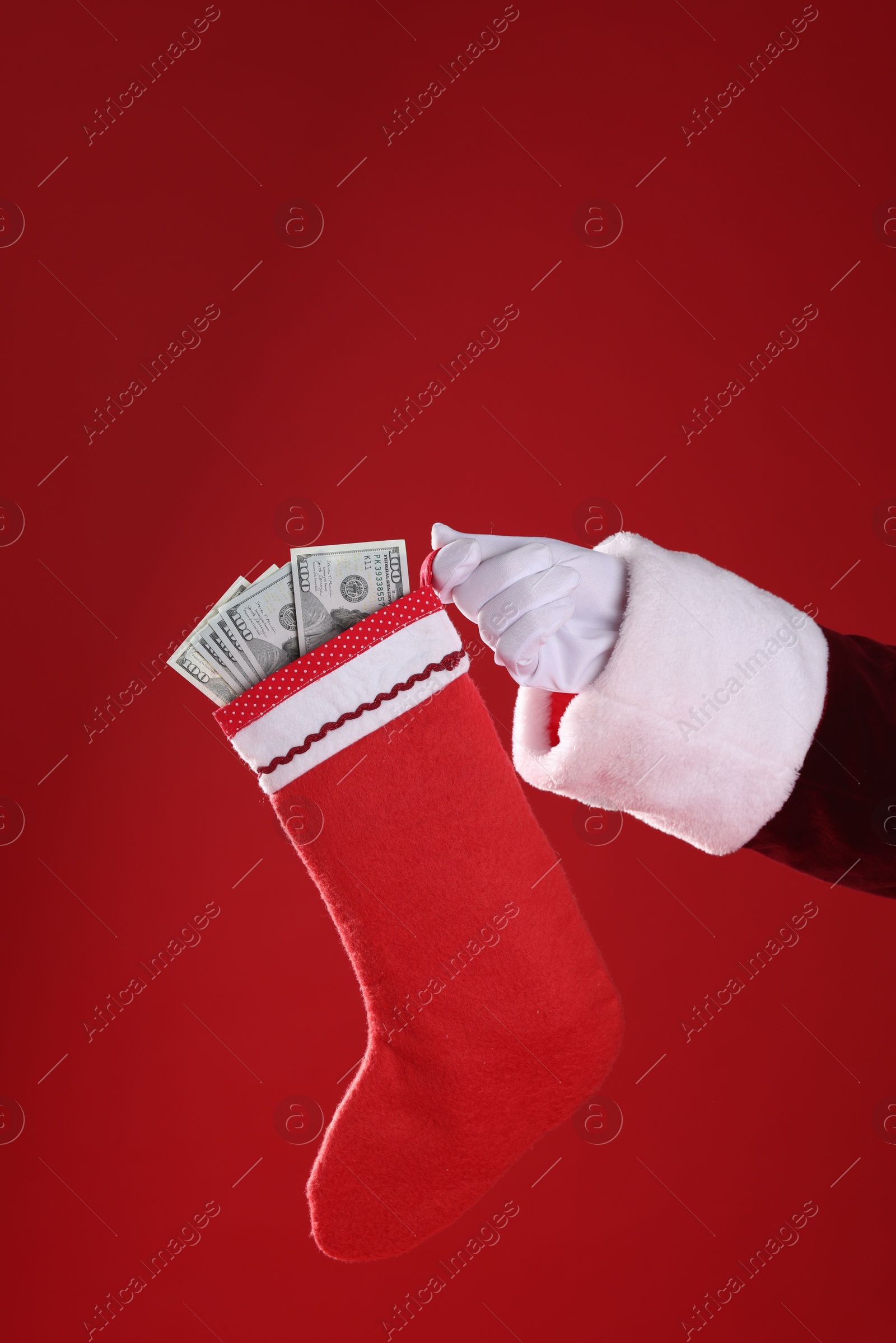 Photo of Santa holding stocking with dollar banknotes on red background, closeup