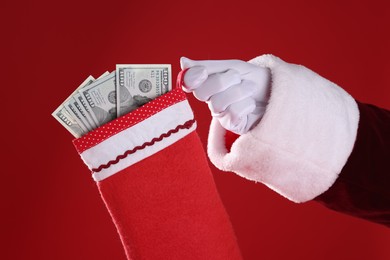 Photo of Santa holding stocking with dollar banknotes on red background, closeup