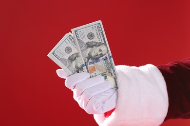 Photo of Santa Claus holding dollar banknotes on red background, closeup