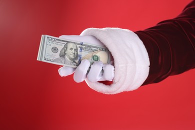 Photo of Santa Claus holding dollar banknotes on red background, closeup