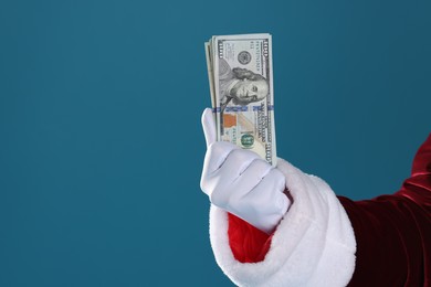 Photo of Santa Claus holding dollar banknotes on blue background, closeup. Space for text