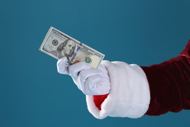 Photo of Santa Claus holding dollar banknotes on blue background, closeup