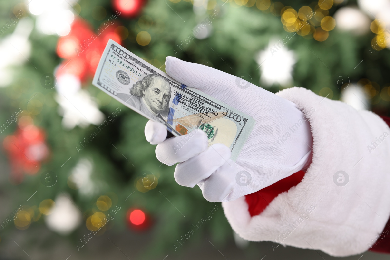 Photo of Santa Claus holding dollar banknotes against blurred Christmas lights, closeup