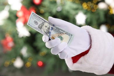 Photo of Santa Claus holding dollar banknotes against blurred Christmas lights, closeup