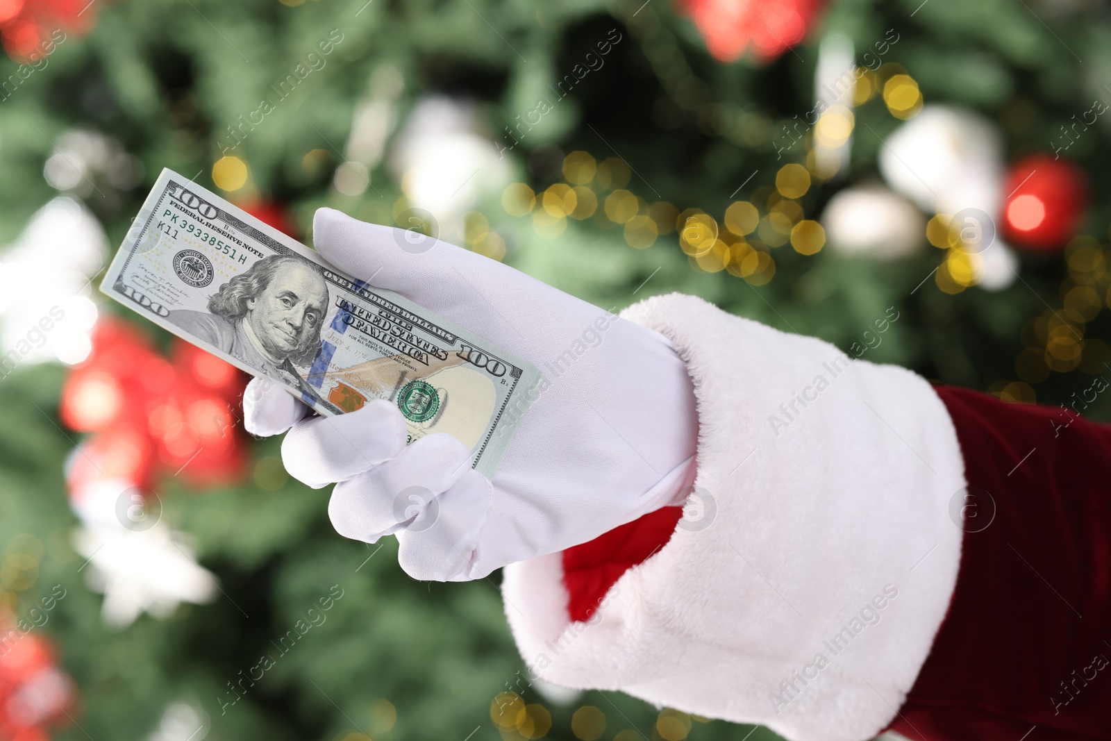 Photo of Santa Claus holding dollar banknotes against blurred Christmas lights, closeup