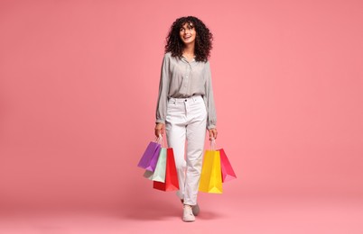 Smiling woman with colorful shopping bags on pink background