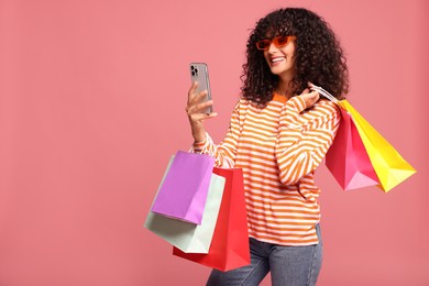 Photo of Smiling woman with colorful shopping bags and smartphone on pink background. Space for text