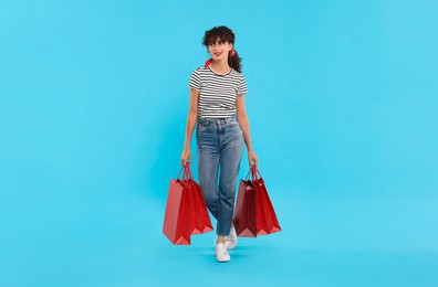 Beautiful woman with shopping bags on light blue background