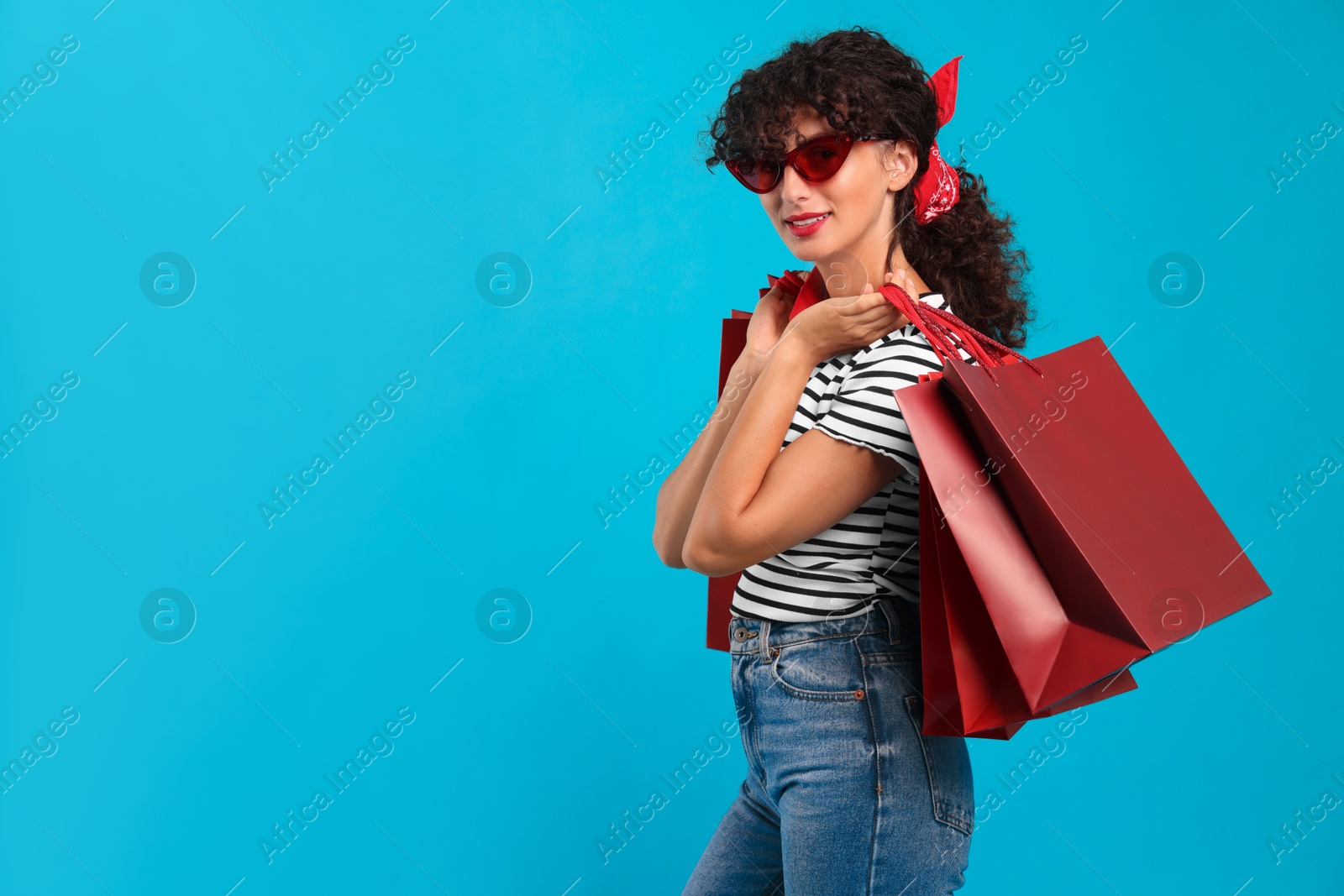 Photo of Smiling woman with shopping bags on light blue background. Space for text