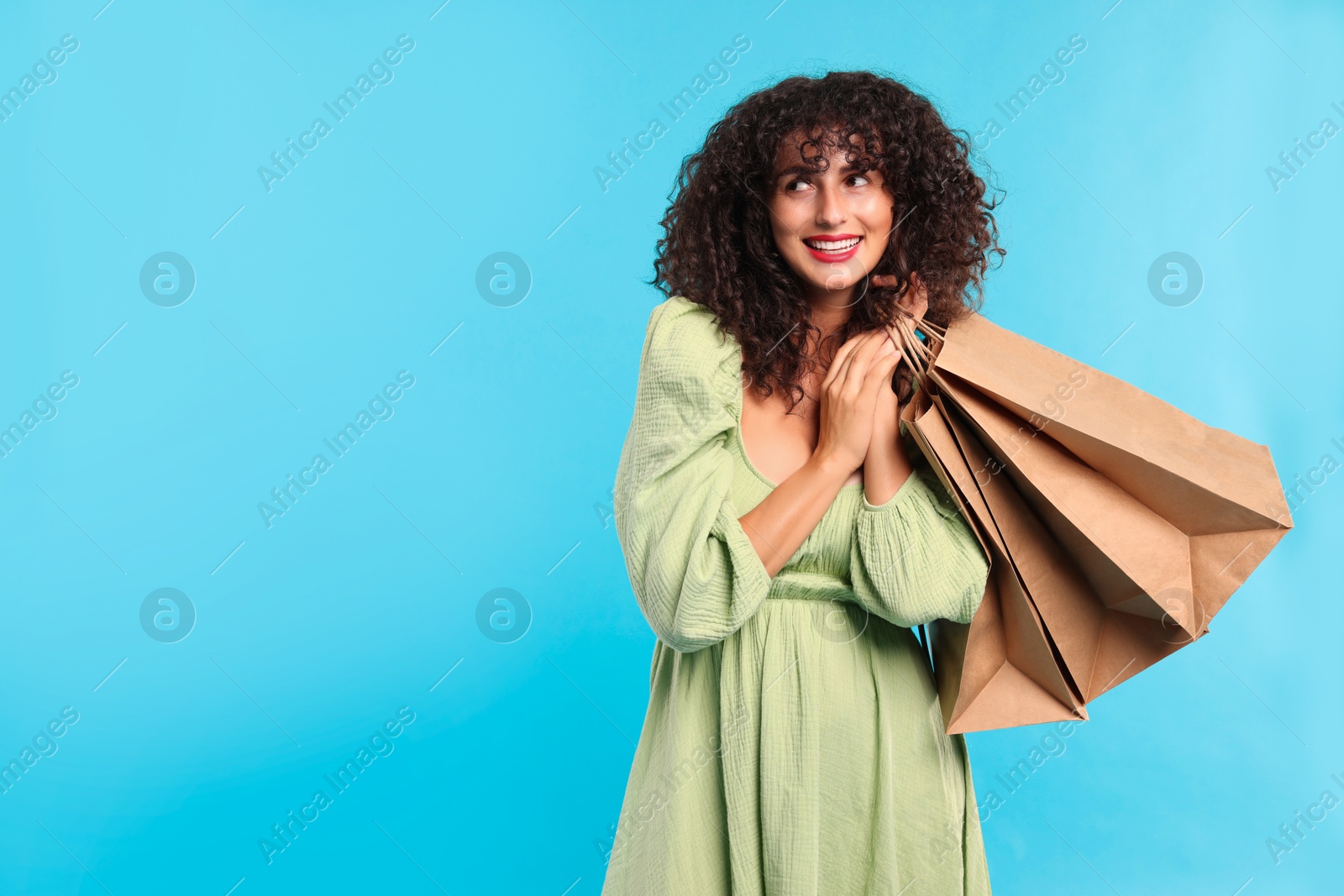 Photo of Smiling woman with shopping bags on light blue background. Space for text