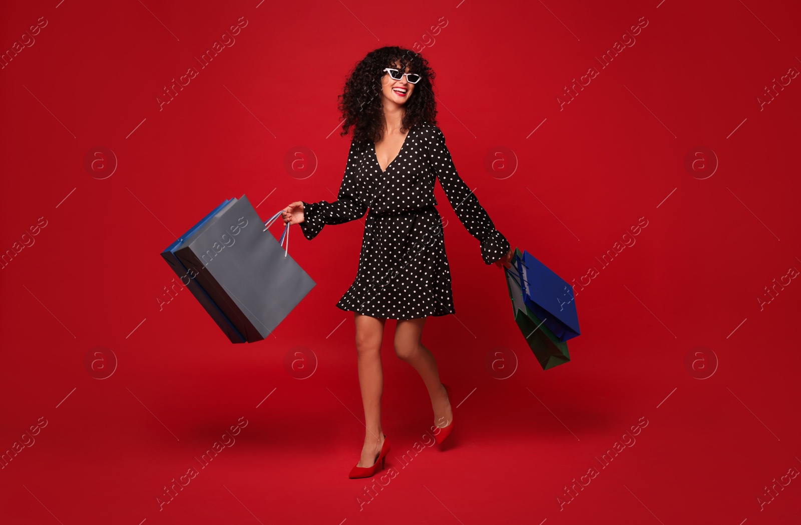 Photo of Smiling woman with colorful shopping bags on red background