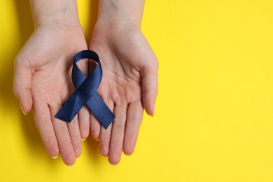 Photo of Woman with dark blue ribbon on yellow background, top view with space for text. Arthritis disease and colon cancer awareness