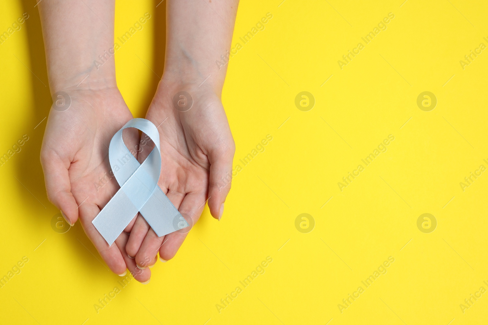 Photo of Woman with light blue ribbon on yellow background, top view and space for text. Childhood cancer awareness