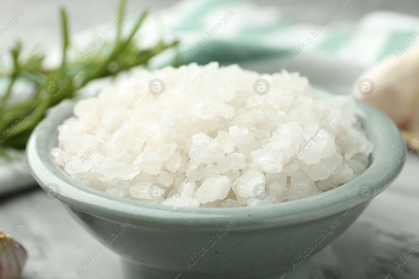 Photo of Sea salt in bowl on gray table, closeup