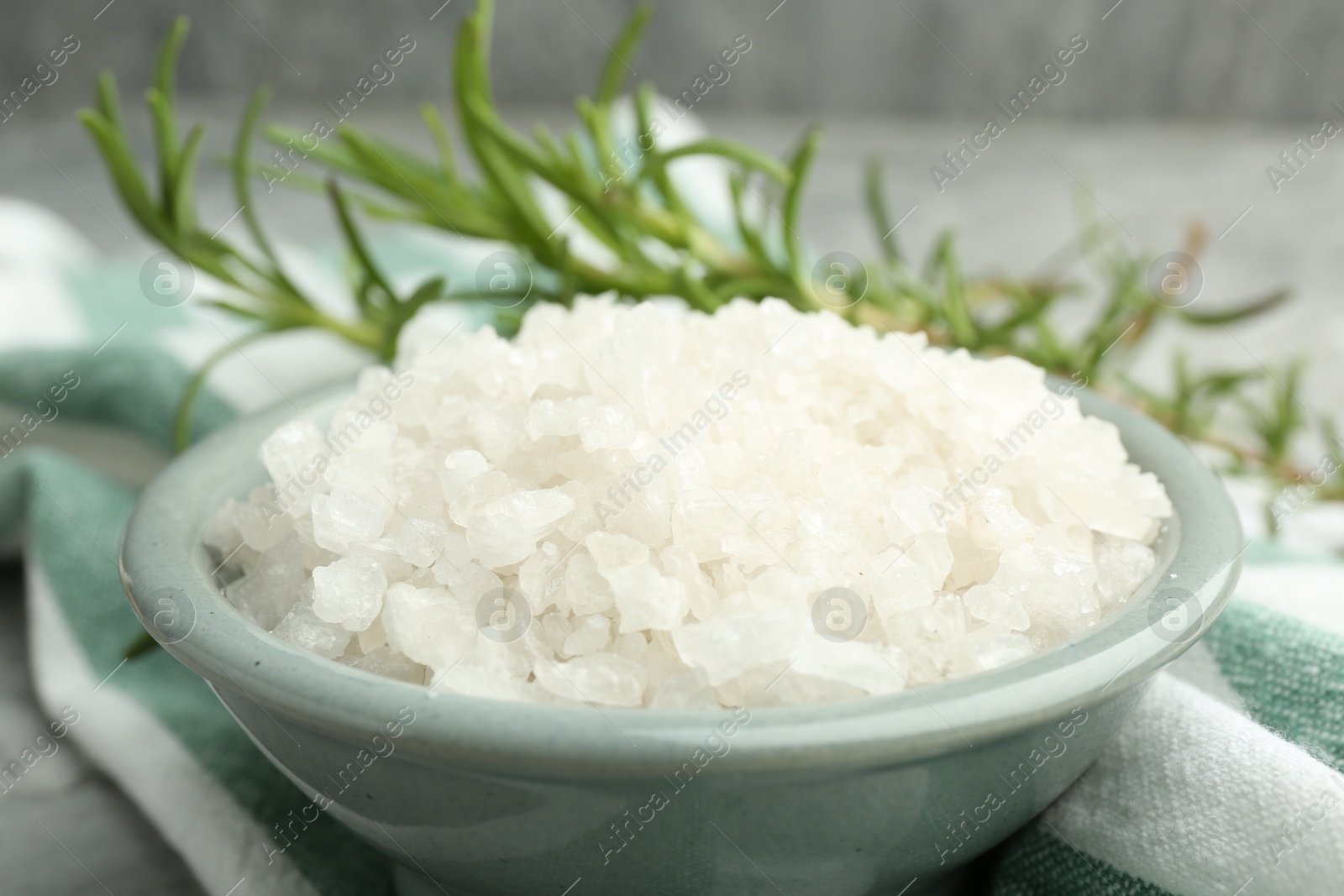 Photo of Sea salt in bowl and rosemary on table, closeup