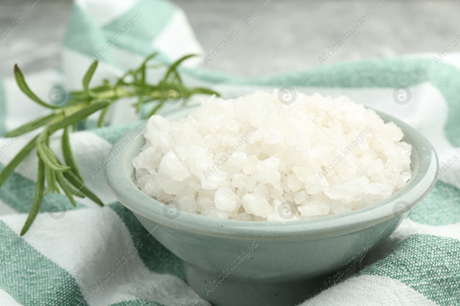 Photo of Sea salt in bowl and rosemary on table, closeup