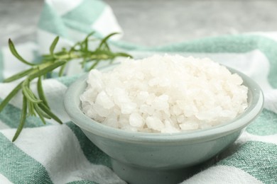 Sea salt in bowl and rosemary on table, closeup