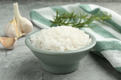 Photo of Sea salt in bowl on gray textured table, closeup