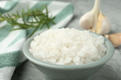 Photo of Sea salt in bowl on gray table, closeup