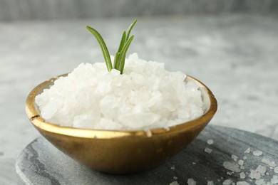 Photo of Sea salt and rosemary in bowl on gray table, closeup