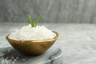 Photo of Sea salt and rosemary in bowl on gray textured table, closeup. Space for text