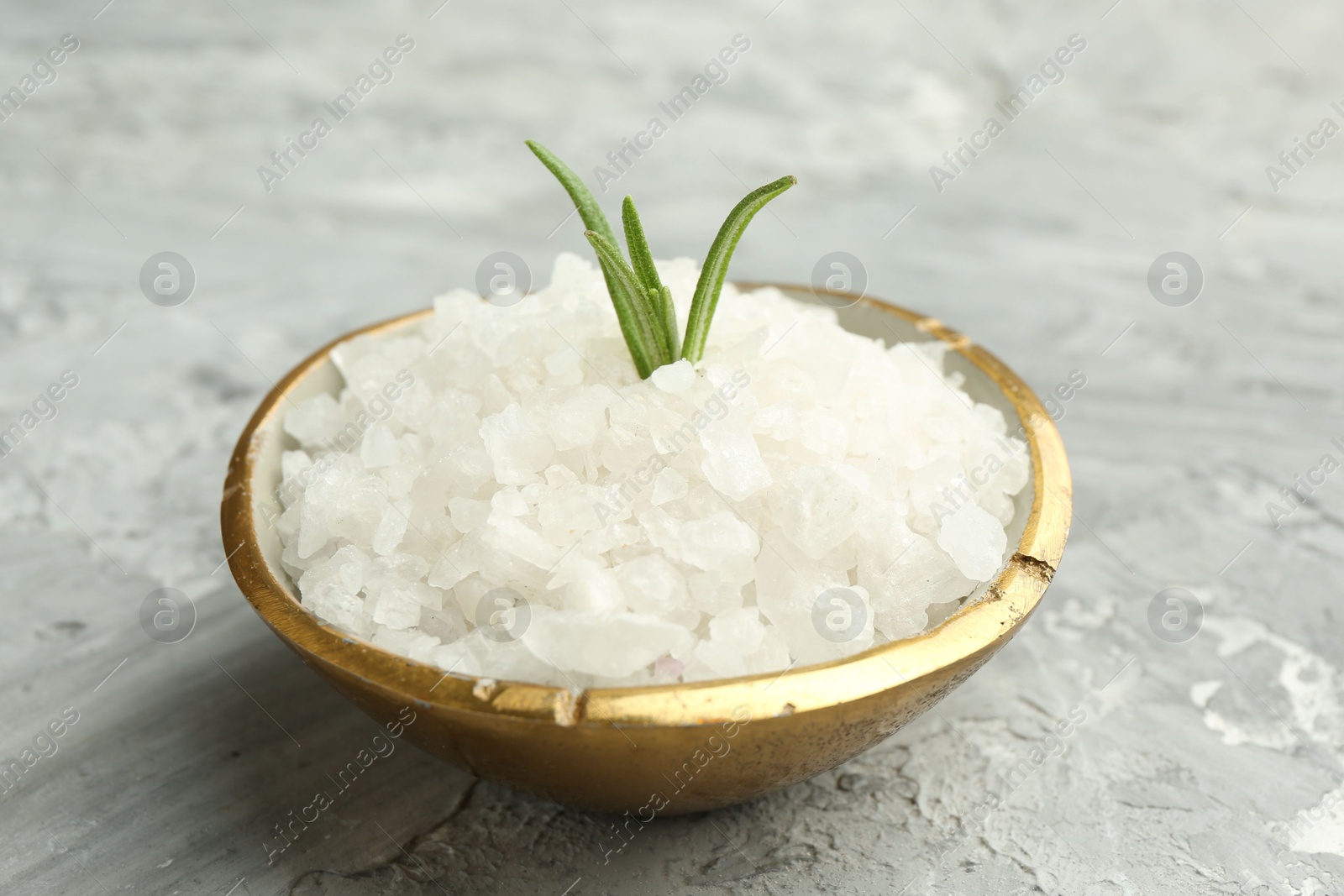 Photo of Sea salt and rosemary in bowl on gray textured table, closeup