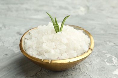 Photo of Sea salt and rosemary in bowl on gray textured table, closeup