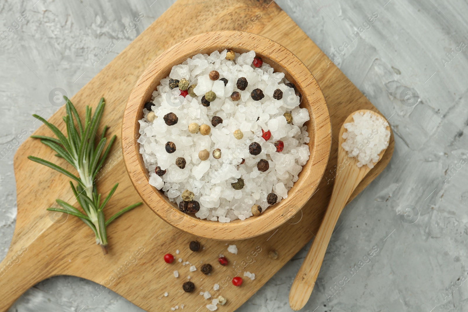 Photo of Sea salt and spices in bowl on gray textured table, top view