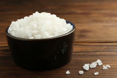 Photo of Sea salt in bowl on wooden table, closeup