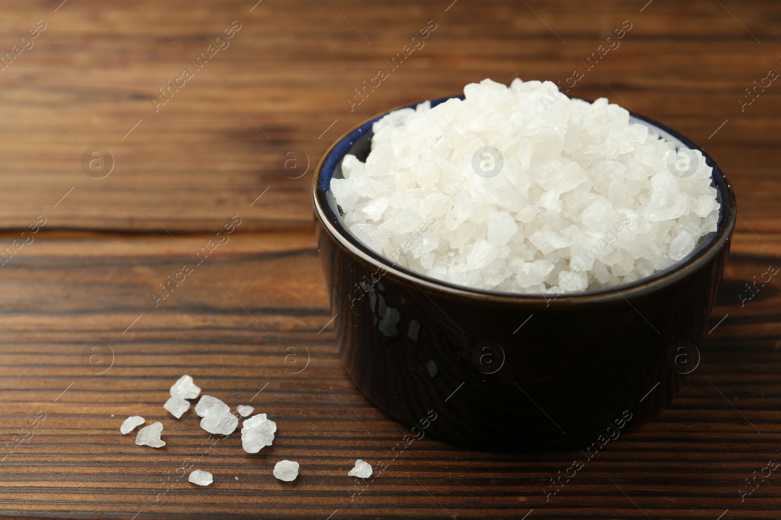 Photo of Sea salt in bowl on wooden table, closeup