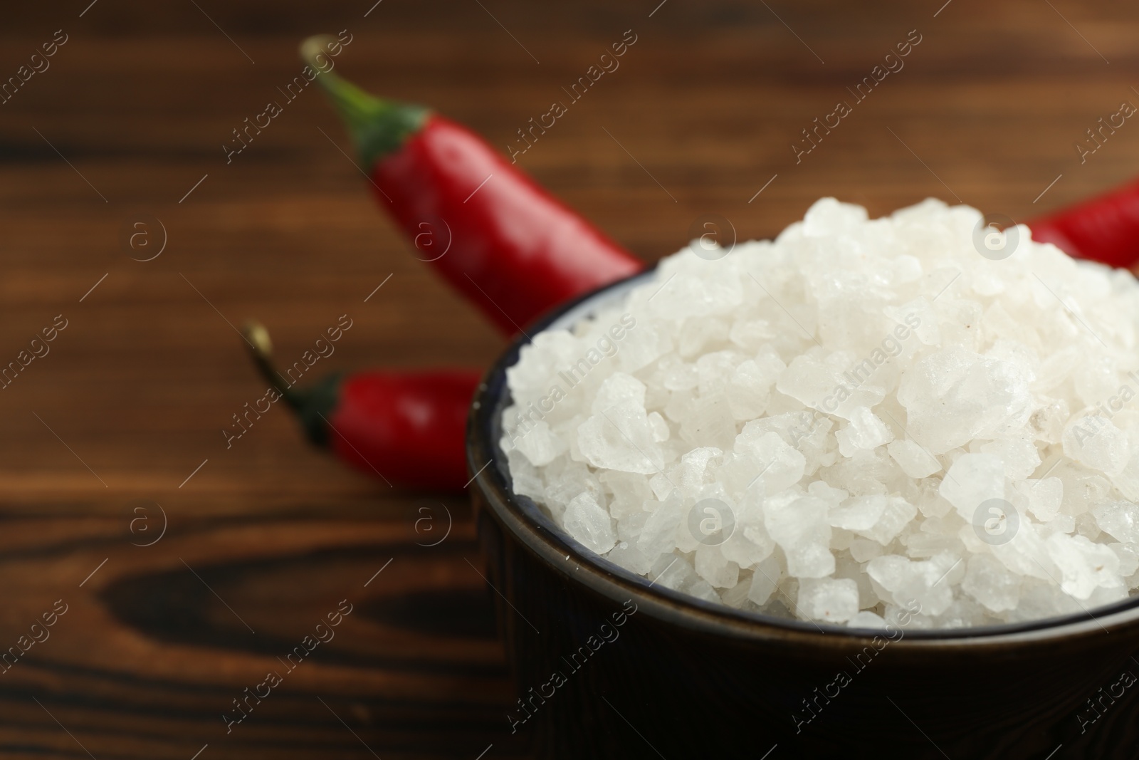 Photo of Sea salt in bowl on wooden table, closeup