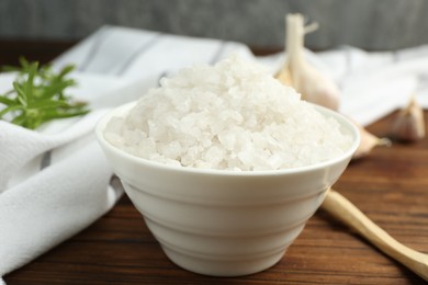 Photo of Sea salt in bowl on wooden table, closeup