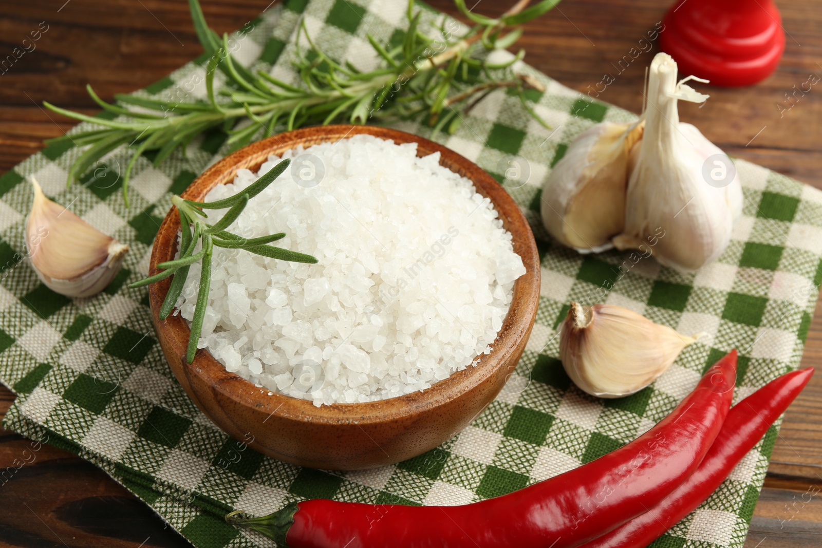 Photo of Sea salt in bowl and spices on wooden table, closeup