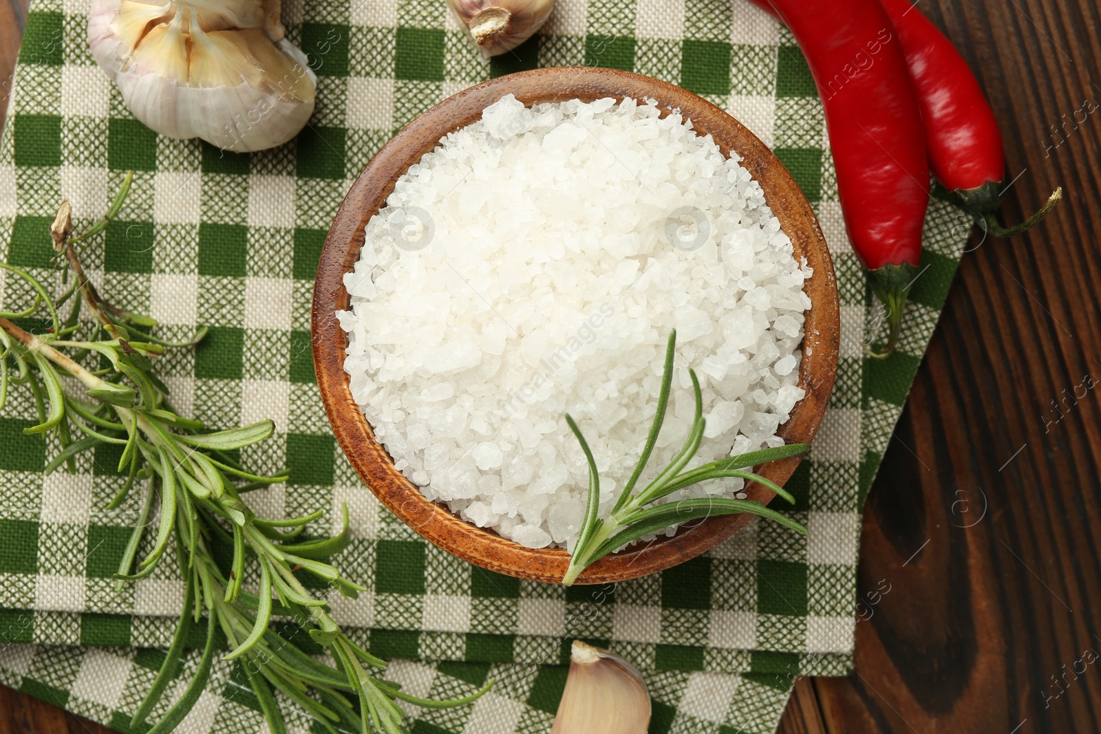 Photo of Sea salt in bowl and spices on wooden table, flat lay