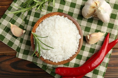 Sea salt in bowl and spices on wooden table, flat lay