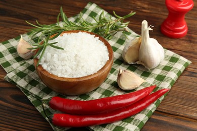 Photo of Sea salt in bowl and spices on wooden table, closeup